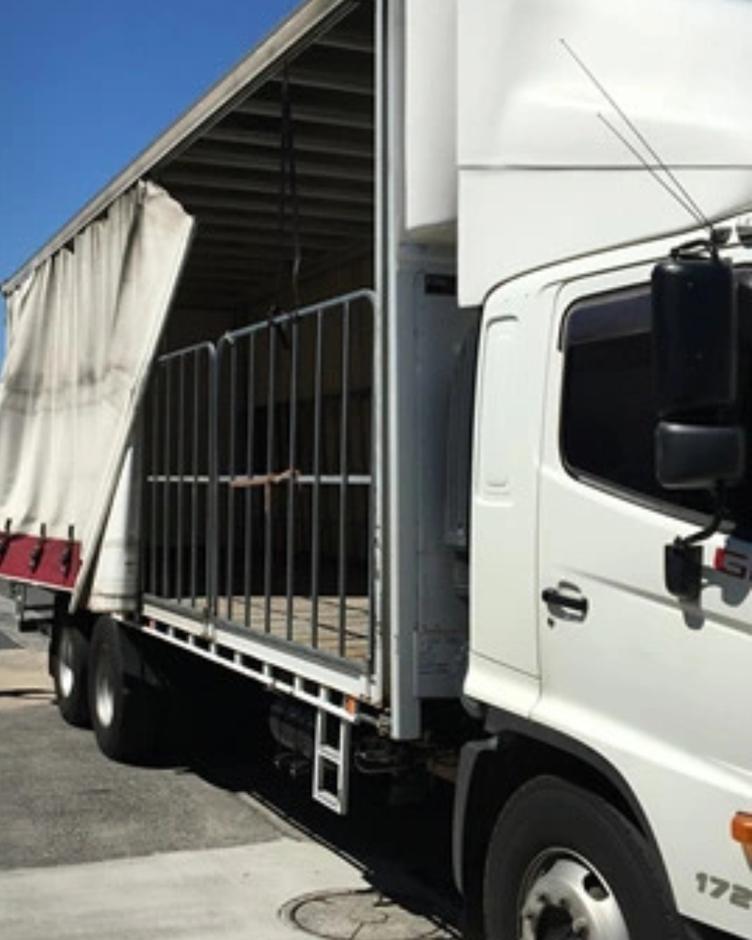 White delivery truck with curtain-sided trailer and metal safety rails parked under blue sky.